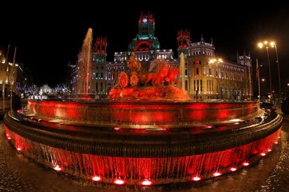 La Cibeles iluminada de rojo. Al fondo el Palacio de Cibeles, uno de los espacios en los que resonarán los villancicos de una decena de coros madrileños del 21 de diciembre al cuatro de enero.