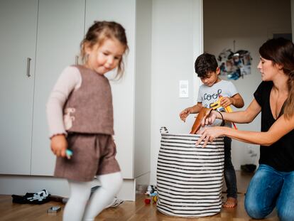 Dos niños con su madre recogen los juguetes del cuarto.