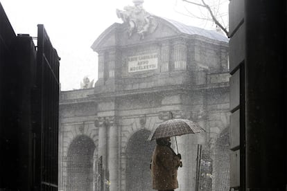 Una mujer camina por delante de la Puerta de Alcalá durante la nevada de ayer por la mañana.