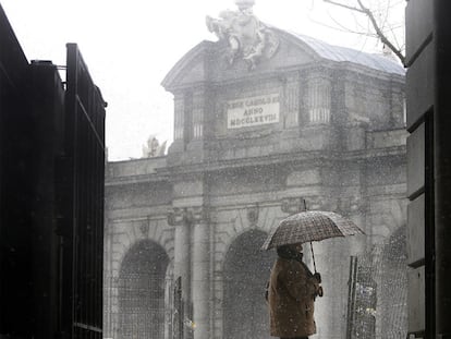 Una mujer camina por delante de la Puerta de Alcalá durante la nevada de ayer por la mañana.