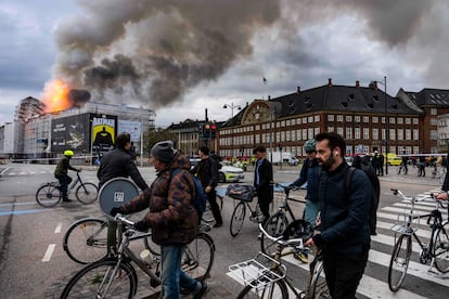 Varias personas pasan con sus bicicletas cerca del edificio incendiado, este martes en Copenhague.