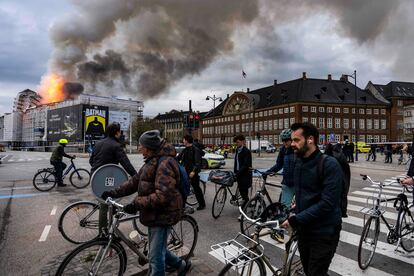 Varias personas pasan con sus bicicletas cerca del edificio incendiado, este martes en Copenhague.