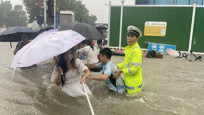 Un agente de policía de tráfico guía a los residentes para cruzar una calle inundada con una cuerda, en Zhengzhou.