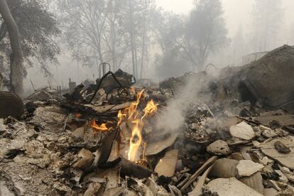 Algunas flamas se elevan entre los restos de una casa consumida por el incendio.