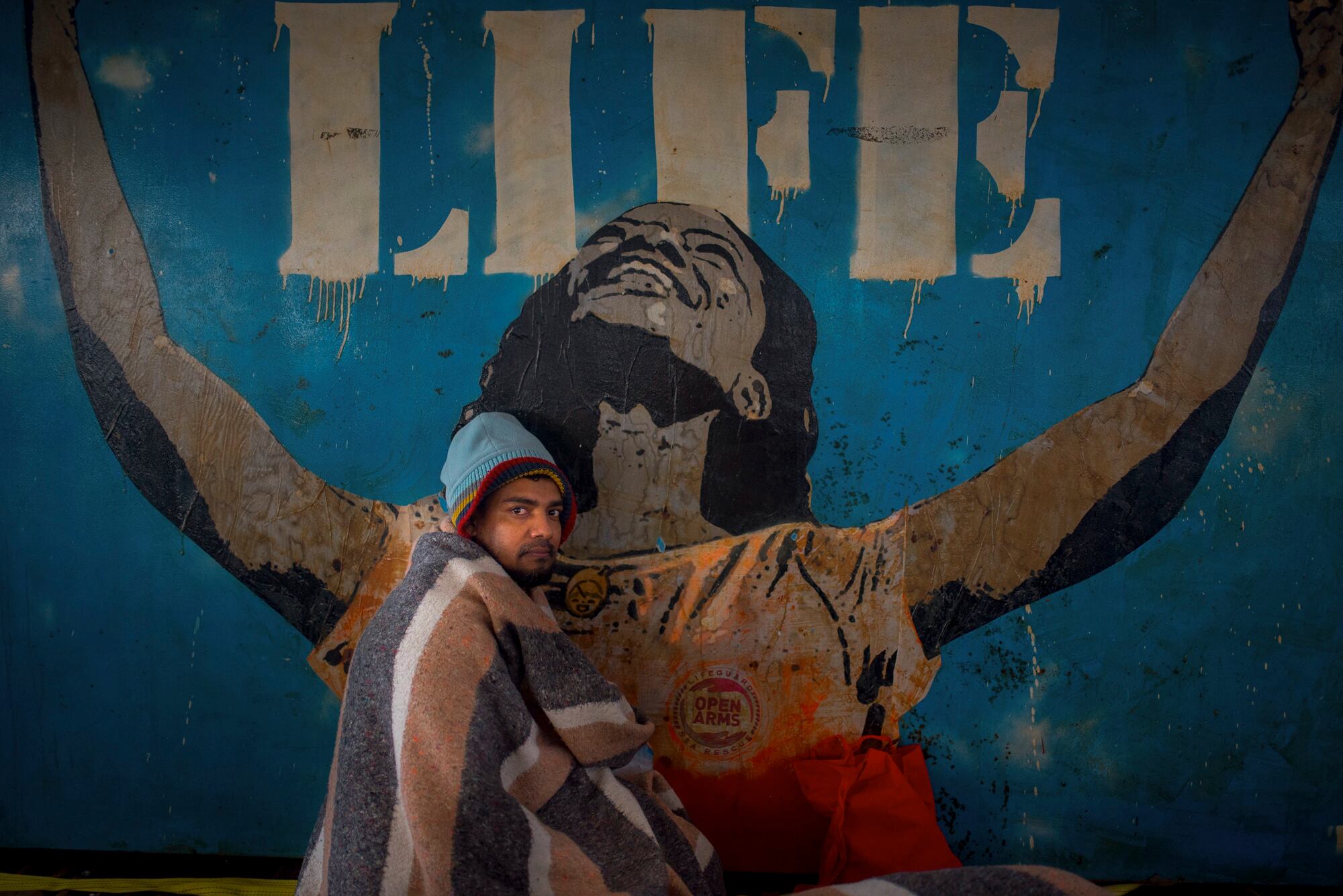 Un joven migrante de Bangladés en la cubierta del Open Arms, junto al grafiti regalado por el artista callejero TV Boy, que representa abrir los brazos a la vida y a la esperanza.