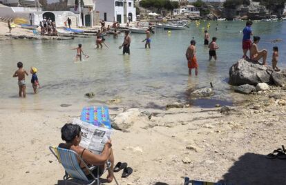 Una mujer lee el peri&oacute;dico en la Cala de Alcafar en Menorca.