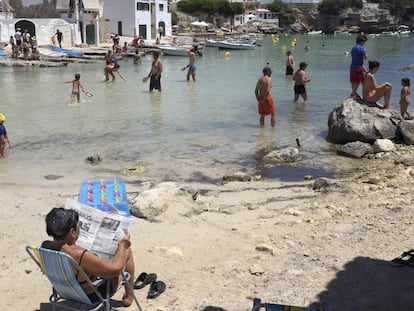 Una mujer lee el periódico en la Cala de Alcafar en Menorca.