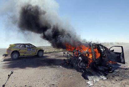 Un coche conduce a pocos metros del coche en llamas de los pilotos Bauyrzhan Issabayev y Gabdulla Ashimov de Kazajstán durante la segunda etapa del Rally Dakar 2014, desde San Luis a San Rafael 
