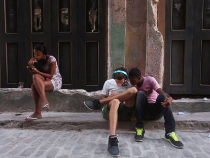 Tres j&oacute;venes utilizan sus tel&eacute;fonos m&oacute;viles para conectarse a Internet en La Habana.