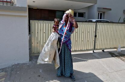 Sarta Kalara holds her 15-month-old Shivani as one end of a barrier tape is tied to Shivani's ankle to prevent her from running away when Kalara works at a construction site nearby in Ahmedabad, India, April 20, 2016. Kalara says she has no option but to tether her daughter Shivani to a stone despite her crying, while she and her husband work for 250 rupees ($3.8) each a shift digging holes for electricity cables in the city of Ahmedabad. There are about 40 million construction workers in India, at least one in five of them women, and the majority poor migrants who shift from site to site, building infrastructure for India's booming cities. Across the country it is not uncommon to see young children rolling in the sand and mud as their parents carry bricks or dig for new roads or luxury houses. REUTERS/Amit Dave       SEARCH "TIED TODDLER" FOR THIS STORY. SEARCH "THE WIDER IMAGE" FOR ALL STORIES