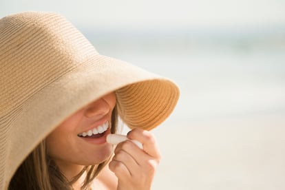 USA, New York State, Rockaway Beach, Woman wearing sun hat applying lipstick