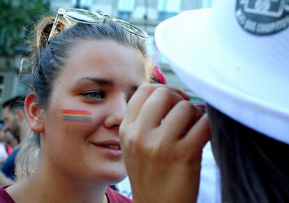 Una joven pinta los colores de la bandera del Orgullo Gay en la cara de otra chica.