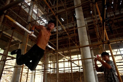 Worker Shi Shenwei performs a high bar routine on a scaffolding as his cousin films, at the construction site of a Buddhist temple in the village of Huangshan, near Quanzhou, Fujian Province, China, September 28, 2016. REUTERS/Thomas Peter        SEARCH "BRICK CARRIER" FOR THIS STORY. SEARCH "WIDER IMAGE" FOR ALL STORIES. 