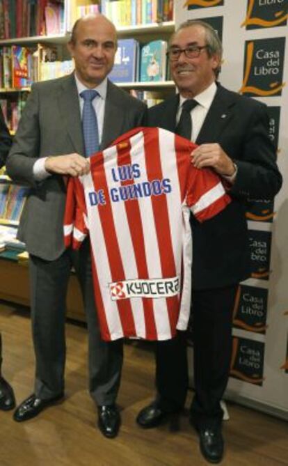 El ministro de Econom&iacute;a, Luis de Guindos (i) y el exjugador del Atl&eacute;tico de Madrid Adelardo Rodr&iacute;guez, muestran una camiseta del club rojiblanco durante la presentaci&oacute;n del libro &quot;100 motivos para ser del Atleti&quot;, escrito por el periodista de la Agencia EFE Fernando Cast&aacute;n.