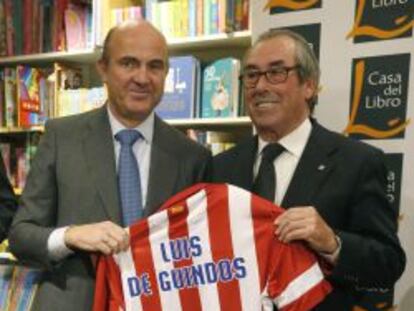 El ministro de Econom&iacute;a, Luis de Guindos (i) y el exjugador del Atl&eacute;tico de Madrid Adelardo Rodr&iacute;guez, muestran una camiseta del club rojiblanco durante la presentaci&oacute;n del libro &quot;100 motivos para ser del Atleti&quot;, escrito por el periodista de la Agencia EFE Fernando Cast&aacute;n.