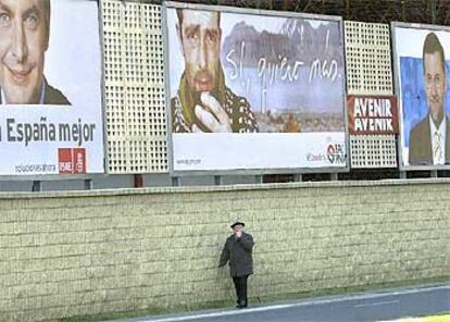 Un anciano pasa junto a unas vallas con propaganda electoral del PSOE, PNV y PP en Bilbao.