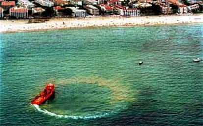 Una embarcación rodea y limpia una de las manchas de petróleo frente a las playas de Salou.