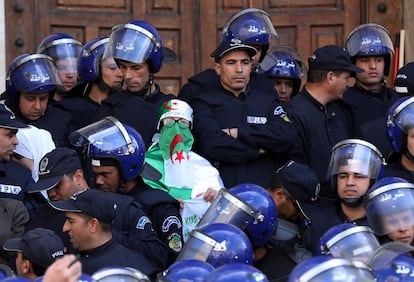Una mujer argelina vestida con la bandera nacional y rodeada por agentes antidisturbios, participa en una protesta contra el presidente interino, Abdelkader Bensalah, el viernes 12 de abril en Argel (Argelia).
