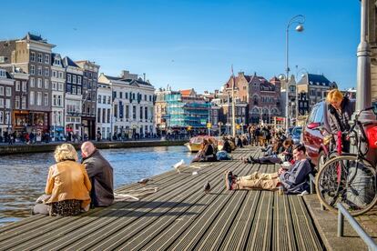 Decenas de turistas descansas a orillas de uno de los canales de Ámsterdam.