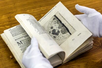 La directora técnica de la biblioteca, con guantes, muestra páginas del atlas lunar.