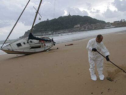 Un operario limpiaba ayer de chapapote la playa de La Concha, junto a un velero que dejó varado el temporal.