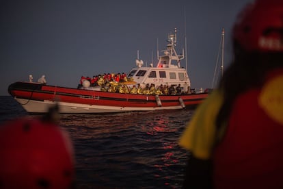 Anochece cuando la Guardia Costera Italiana recoge a los rescatados para trasladarlas a Lampedusa, Italia. Sus tripulantes, enfundados en Equipos de Protección Personal, realizan la maniobra de traspaso de las personas del bote de goma hacia el barco ante la custodia celosa de Òscar, Laura y Fátima. U
