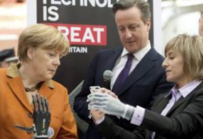 La canciller alemana, Angela Merkel (izda), y el primer ministro británico, David Cameron (dcha), observan el funcionamiento de una mano biónica controlada desde un teléfono móvil hoy en la feria CeBIT en Hannover (Alemania).