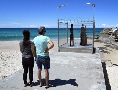 Una pareja observa la escultura que simula una familia en prisión, en la playa de Tamarama.