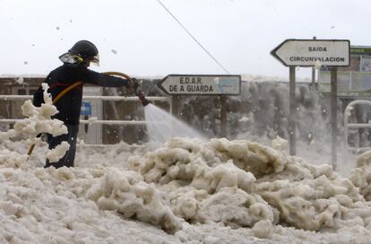 Una borrasca pasará este viernes muy cerca de Galicia, trayendo consigo una situación meteorológica adversa en la tierra y en el mar. En la imagen, un bombero retira la espuma causada por el fuerte oleaje en el puerto de A Garda (Pontevedra). 