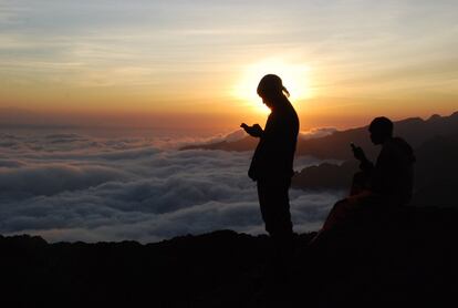 Un guía tanzano en una roca en el camino al Kilimanjaro al atardecer tratando de obtener señal de teléfono móvil.