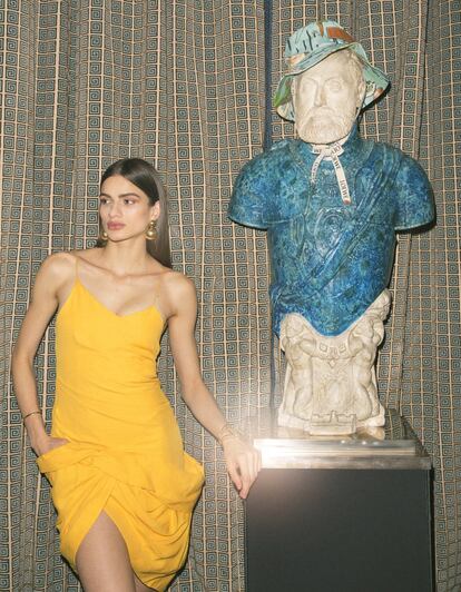 Vestido drapeado amarillo de Jacquemus, pendientes de Helena Rohner, pulsera rígida (en la mano izquierda) de Tous y brazalete de Glenda López. Sobre la estatua, gorro estampado de Loewe Paula’s Ibiza.