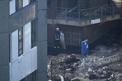 Homem olha os danos causados pelo incêndio junto a um bombeiro próximo à Torre Grenfell.