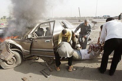 Iraquíes extraen el cadáver de un hombre muerto ayer al explotar un coche bomba en una carretera cerca de Bagdad.