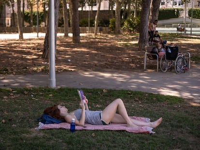 Una mujer lee en el césped del parque de la España Industrial, en Barcelona.