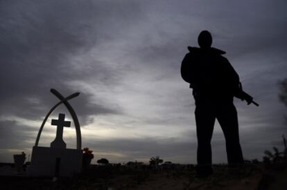 El lunes 25 de octubre fueron enterrados en Ciudad Juárez las 14 víctimas mortales del asesinato perpetrado el viernes, durante una fiesta de cumpleaños. Muchas de las víctimas eran menores de edad. En la imagen, un policía custodia el cementerio, ante las amenazas por parte de los sicarios de que el cortejo fúnebre iba a ser tiroteado-