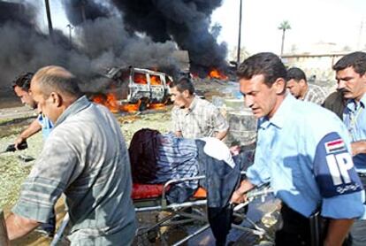 La policía iraquí evacua a un herido ante la sede de la Cruz Roja, con la ambulancia bomba aún en llamas.