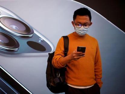 Un joven consulta su iPhone 12 frente a una tienda de Apple en Shanghái.