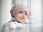 Una niña con cáncer mira por la ventana.