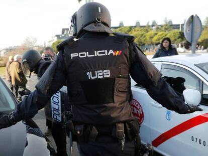 Efectivos de la Polic&iacute;a Nacional entre un veh&iacute;culo de licencia VTC y un taxi a las puertas del recinto ferial de IFEMA.