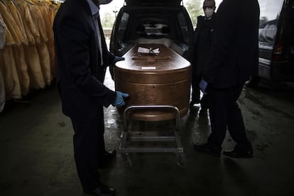 Personal del Tanatorio M30 mete un féretro en un coche fúnebre.