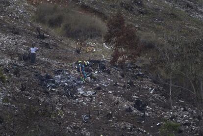Un agente de la Guardia Civil camina entre restos del helicóptero sobre la tierra quemada a causa de la colisión.