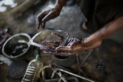 Un campesino birmano, con las manos llenas de crudo, arregla la maquiaria que utiliza para las extracciones.