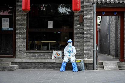 Un sanitario equipado con un traje de protección contra la covid descansa frente a un restaurante cerrado en Pekín (China). 
