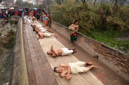 Un grupo de devotos hindúes rueda sobre el suelo durante una ofrenda tras un ritual de baño en el último día del Festival Swasthani, en el río Hanumante en Bhaktapur, a las afueras de Katmandú (Nepal).