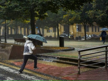 Un peatón cruza una calle entre una fuerte tromba de agua en Pamplona.