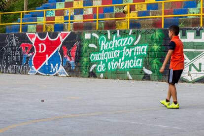 Un niño juega al fútbol en una pista de deportes de la Comuna 13 de Medellín. En sus paredes hay varios murales y uno de ellos dice 'Rechazo cualquier forma de violencia'. 