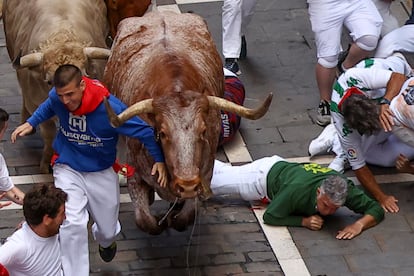 Varios mozos caen al suelo al paso de los toros de la ganadería de Jandilla por la calle Estafeta, este viernes durante el sexto encierro de los Sanfermines. 