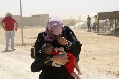 Una refugiada siria lleva a su hijo en brazos mientras camina entre una tormenta de arena en el campo de refugiados de Al Zaatr, en Mafraq (Jordania), cerca de la frontera con Siria, donde se desarrolla una guerra civil. Agosto 2012.