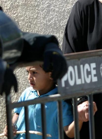 Un niño de una de las familias coge la mano de su madre tras el cordón policial