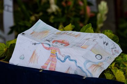 El dibujo de un bombero hecho por un niño, colocado entre los arreglos florales alrededor de las urnas.
